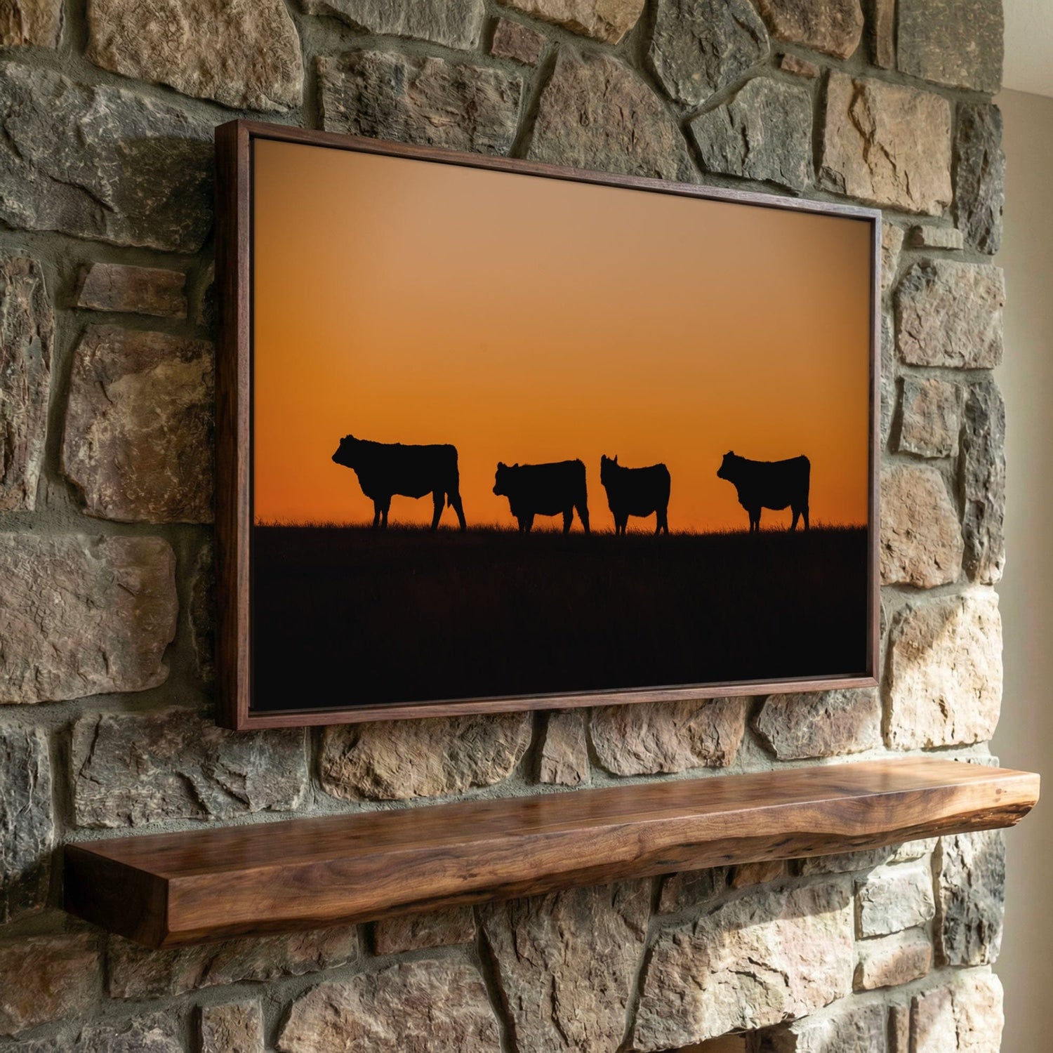 minimalist cattle wall art silhouette of black angus cattle in front of an orange sunset, canvas is hanging on rock fireplace.
