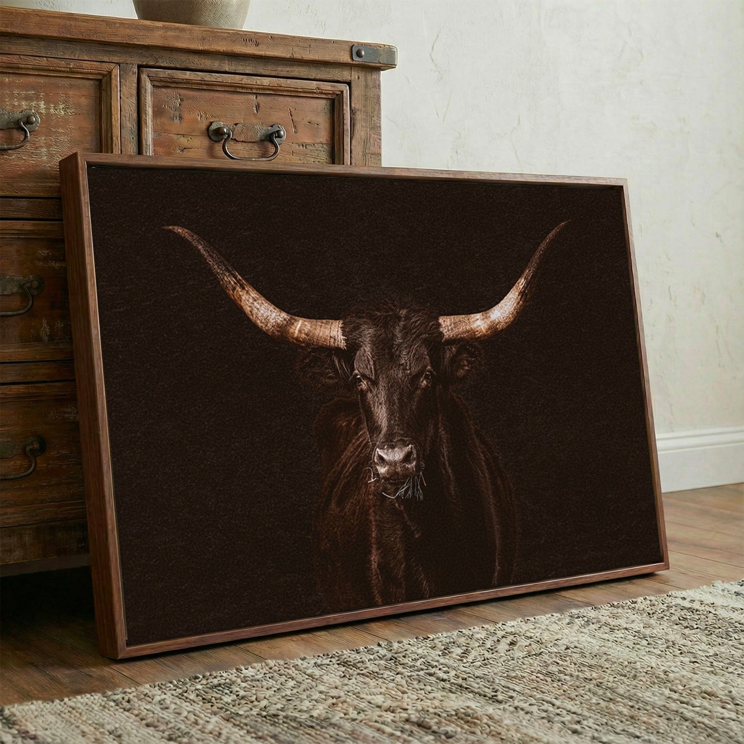 gothic western wall art canvas print of a black longhorn cow on black background. showing leaning against a rustic brown wooden cabinet.